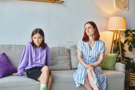 frustrated woman and offended preteen daughter sitting on couch in living room, generation gap