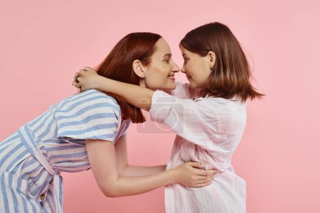 Téléchargez les photos : Vue latérale de la mère gaie et de la fille préadolescente posant face à face sur la famille rose et heureuse - en image libre de droit