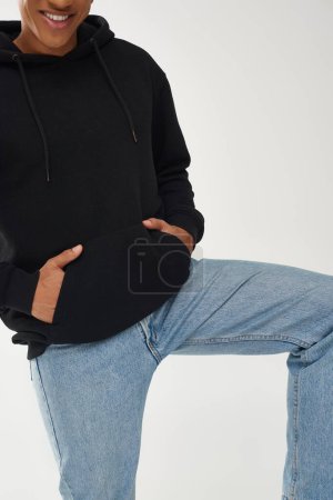 trendiges afrikanisch-amerikanisches Männermodel in lässigem schwarzen Kapuzenpulli und Jeans, Kopierfläche für Werbung