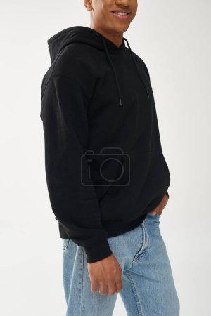 trendiges afrikanisch-amerikanisches Männermodel in lässigem schwarzen Kapuzenpulli und Jeans, Kopierfläche für Werbung