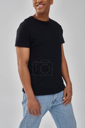 modelo masculino afroamericano elegante posando en camiseta negra y pantalones vaqueros, espacio de copia para la publicidad
