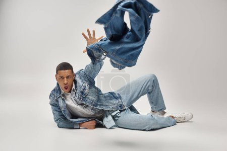 attractive emotional african american man in stylish denim outfit posing in motion, fashion concept