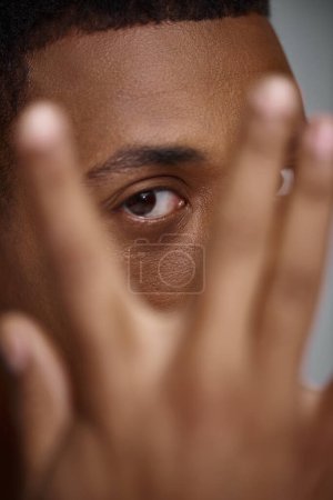 Nahaufnahme eines hübschen, ansprechenden afrikanisch-amerikanischen Mannes mit der Hand vor dem Gesicht, Modekonzept