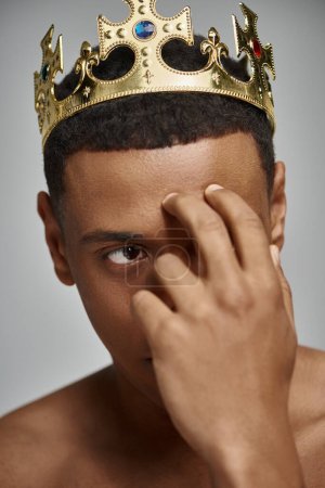 alluring african american man in golden crown posing topless with hand near face, fashion concept