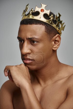 alluring african american man in golden crown posing topless with hand near face, fashion concept