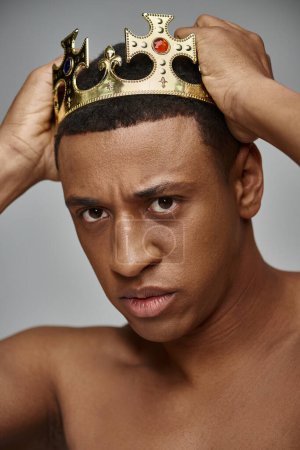 alluring young african american man posing topless with hands on golden crown, fashion concept