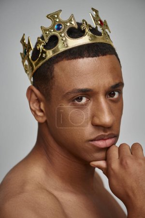 verführerisch afrikanisch-amerikanischer Mann in goldener Krone posiert oben ohne mit händennahem Gesicht, Modekonzept