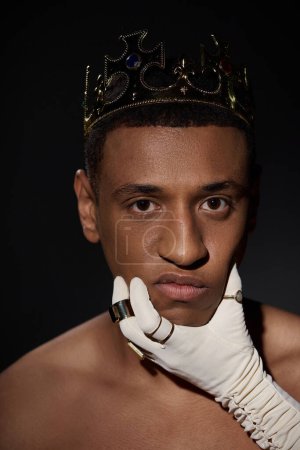 female hand in white glove with rings near face of shirtless african american man with crown