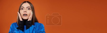 banner of shocked woman with pierced nose touching cheeks with hands and on orange backdrop