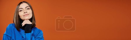 femme coûteuse avec nez percé regardant la caméra tout en pensant sur fond orange, bannière
