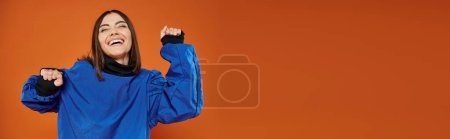 banner of excited woman with pierced nose gesturing and smiling on orange backdrop, blue sweatshirt