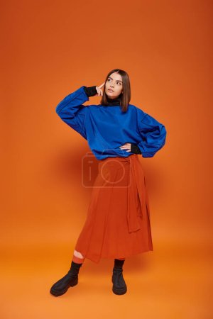 pensive young woman with pierced nose standing in autumn attire with hand on hip on orange backdrop Mouse Pad 680596346
