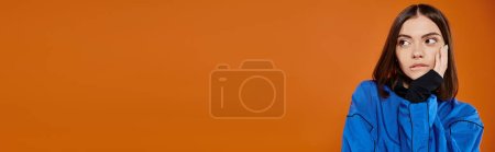 Téléchargez les photos : Bannière de femme coûteuse avec nez percé mordant lèvre et regardant loin sur fond orange - en image libre de droit