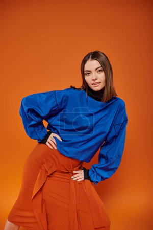Photo for Attractive young woman with pierced nose standing in autumn attire on orange backdrop, hand on hip - Royalty Free Image