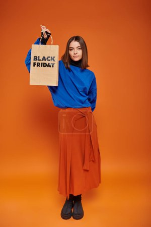 Modische junge Frau in Herbstkleidung und Stiefeln mit Einkaufstasche mit schwarzen Freitagsbriefen