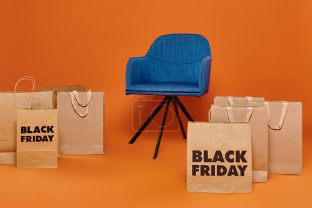 shopping bags with black friday letters near blue velour armchair on orange backdrop, sales season