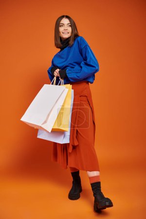 full length of cheerful woman in stylish autumnal clothes holding shopping bags on black friday