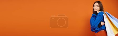 Photo for Banner of positive woman in autumnal clothes holding shopping bags on black friday, orange backdrop - Royalty Free Image