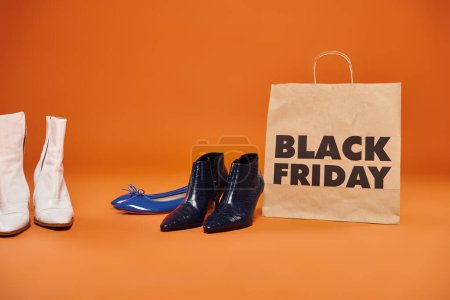 Herbstliche Stiefel und flache Schuhe in der Nähe einer Einkaufstasche mit schwarzen Freitagsbuchstaben auf orangefarbenem Hintergrund