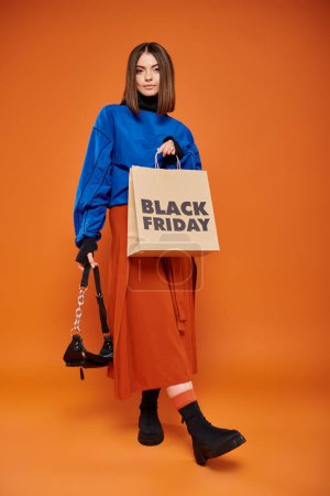 mujer joven en ropa otoñal de pie con bolso de moda y bolso de compras el viernes negro