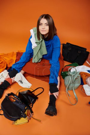 Foto de Mujer joven sentada alrededor de bolsos y ropa de abrigo sobre fondo naranja, concepto de viernes negro - Imagen libre de derechos