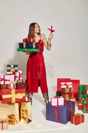 schöne Frau mit Tätowierungen, die Geschenke hält und sich eine davon ansieht, Konzept für Weihnachtsgeschenke