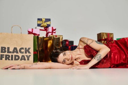 Smiley-Frau blickt in Kamera und liegt auf dem Boden neben Einkaufstasche und Geschenken, schwarzer Freitag