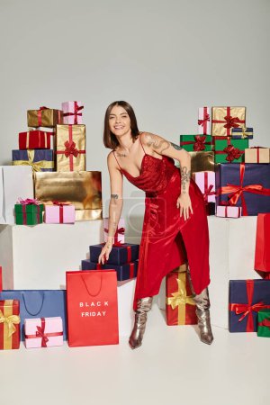 Photo for Attractive lady in red dress leaning forward to pick up red shopping bag, black friday concept - Royalty Free Image