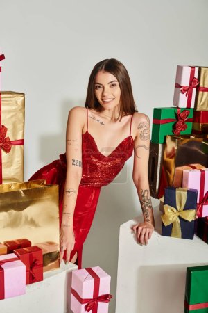 attraktive Frau in festlichem Kleid mit Tätowierungen posiert mit Stapel von Geschenken, Weihnachtsgeschenken Konzept
