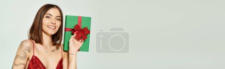 young lady in festive dress holding present and smiling cheerfully, holiday gifts concept, banner