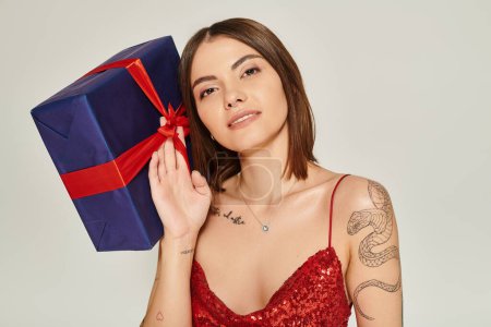 Téléchargez les photos : Belle femme tenant un énorme cadeau et souriant posant sur fond écru, concept de cadeaux de vacances - en image libre de droit
