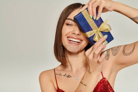 Photo for Attractive lady smiling sincerely with closed eyes with present in front of her face, holiday gifts - Royalty Free Image
