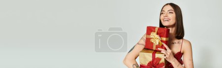 Téléchargez les photos : Femme heureuse avec des cadeaux rouges dans les mains regardant loin sur fond écru, concept de cadeaux de vacances, bannière - en image libre de droit