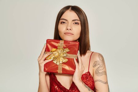 verträumte junge Frau hält rotes Geschenk in der Hand und blickt direkt in die Kamera, Konzept für Weihnachtsgeschenke