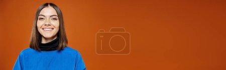 hermosa mujer con la nariz perforada en chaqueta azul casual sonriendo a la cámara en el fondo naranja, pancarta