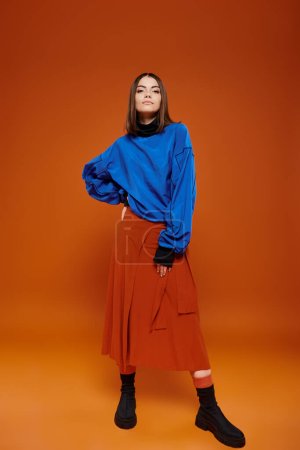 atractiva joven modelo femenino con chaqueta azul casual y falda naranja con su mano en la cadera