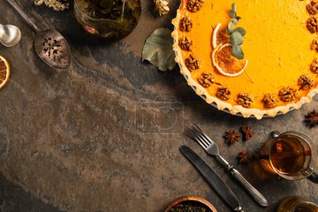 Photo for Delicious pumpkin pie with orange slices and walnuts near vintage cutlery and hot tea on stone table - Royalty Free Image