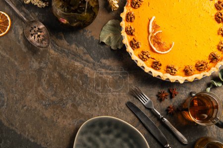 composición de acción de gracias, pastel de calabaza adornado cerca de cubiertos vintage, especias y té en la mesa de piedra