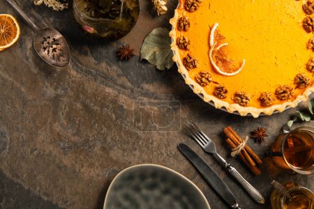 thanksgiving still life, pumpkin pie near vintage cutlery, hot tea and cinnamon on stone surface