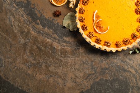 delicious pumpkin pie with orange slices and walnuts near thanksgiving decor on rough stone surface