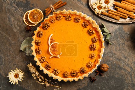 pumpkin pie with walnuts and orange slices near spices, herbs and candles, thanksgiving centerpiece