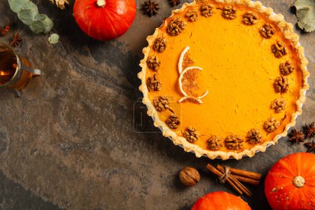 thanksgiving still life, garnished pumpkin pie near ripe pumpkins, herbs and tea on stone surface