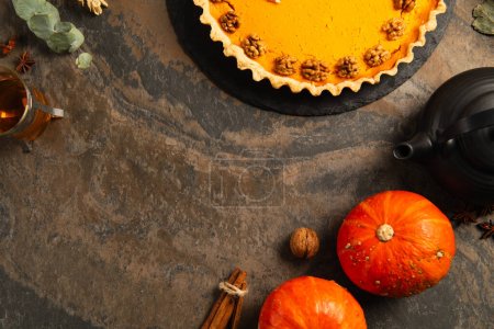 thanksgiving pumpkin pie with walnuts near ripe orange gourds, spices and warm tea on stone table