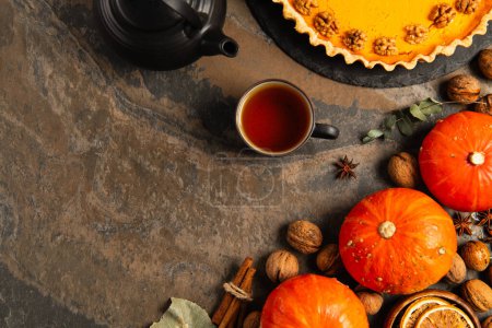 inviting thanksgiving setting, delicious pumpkin pie near hot tea, ripe orange pumpkins and walnuts