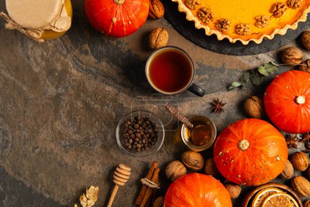 thanksgiving still life, pumpkin pie near ripe gourds, tea with honey and spices on stone backdrop