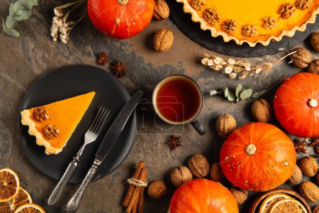 pumpkin pie on black plate near warm tea and ripe pumpkins on stone table with thanksgiving decor