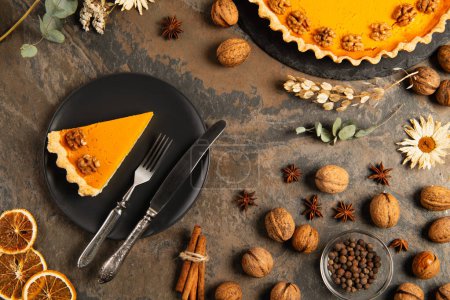 tasty pumpkin pie and cutlery on black ceramic plate near orange gourds on stone table, thanksgiving