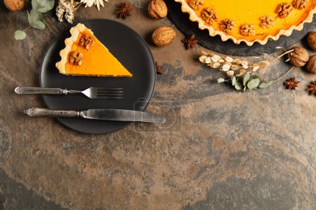 thanksgiving backdrop, black plate with pumpkin pie and cutlery near walnuts and spices with herbs
