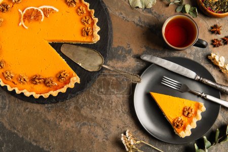 thanksgiving pumpkin pie with walnuts and orange slices near vintage cutlery on rustic stone table