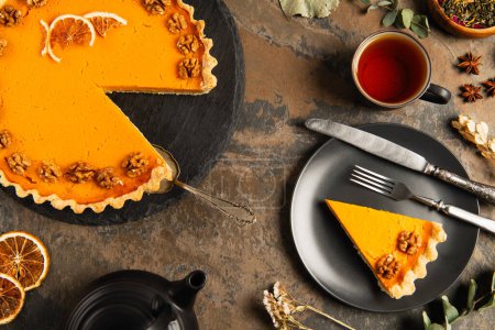 pumpkin pie and vintage cutlery on black plate near tea and herbs on stone surface, thanksgiving